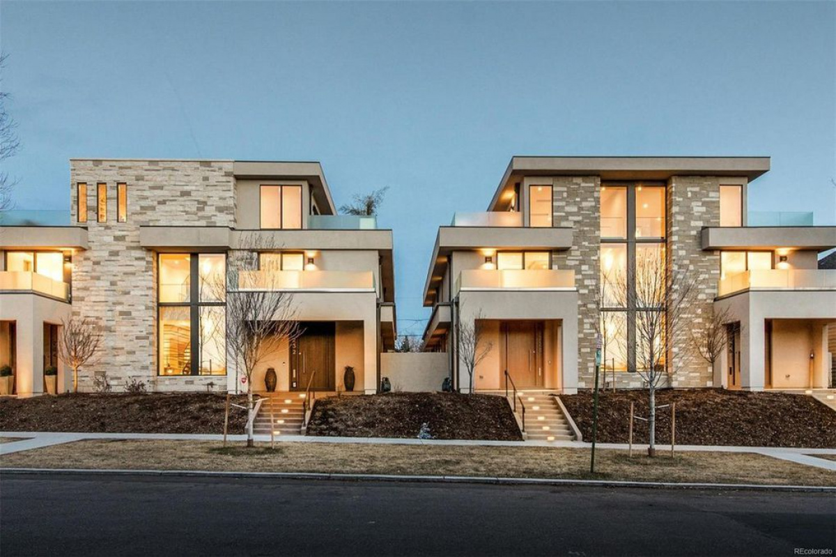 Pair of contemporary stone and stucco homes with tall windows lit at dusk