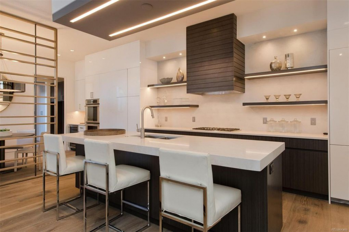 Kitchen with white waterfall island, bar stools and dark range hood