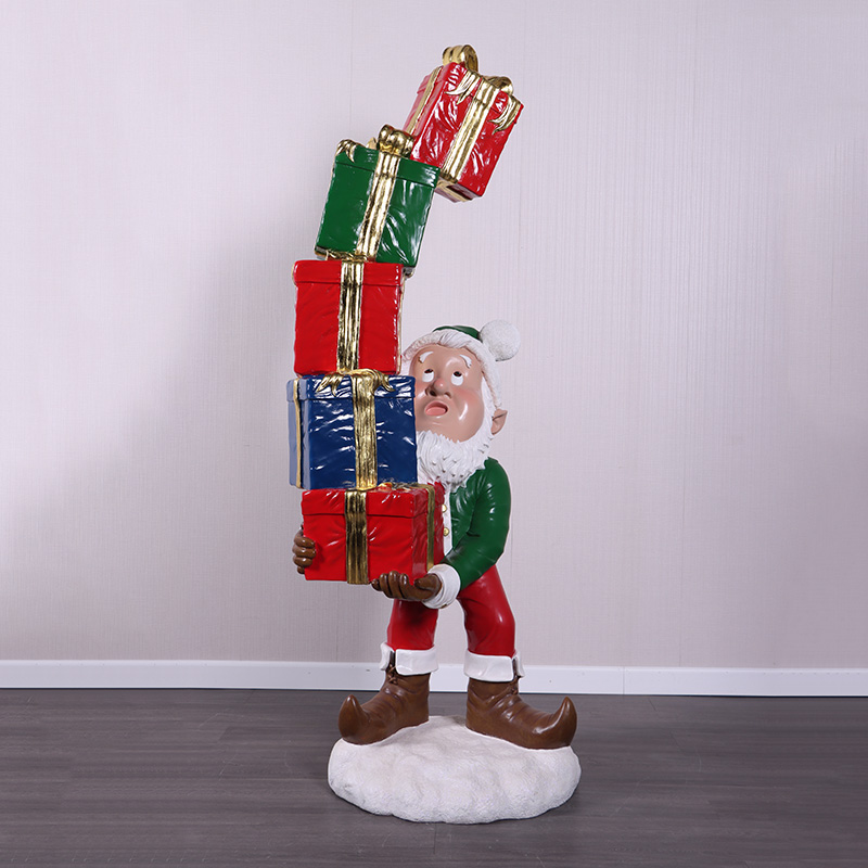Christmas elf figurine holding a tall stack of colorful wrapped presents with gold ribbons.