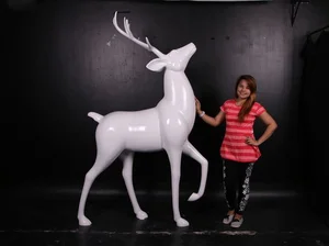 Woman in striped shirt standing next to a large white stag sculpture against a black background.