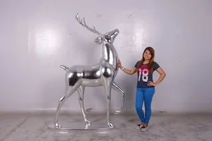 Woman with hand on large shiny silver deer stag sculpture against a plain wall.