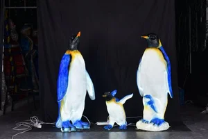 Two adult and one baby penguins standing on a stage with a black backdrop.