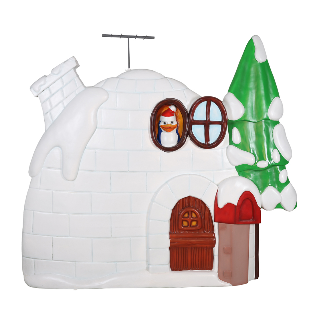 Snow-covered igloo with a penguin in a Santa hat visible through a round window and a green tree.