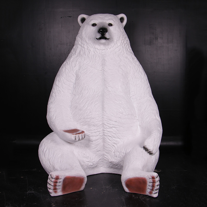 Large white polar bear statue sitting upright with it's paw functioning as a seat against a black background.
