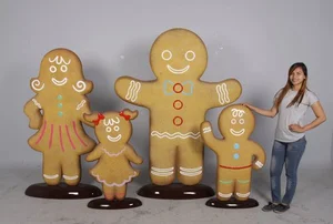 Woman standing next to four large gingerbread family figures of varying sizes with icing decorations.