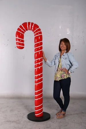 Woman standing beside a large red candy cane prop with white stripes on a round black base.