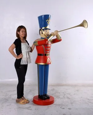 Woman standing next to a large toy hornblower statue playing a horn with a blue and red uniform.