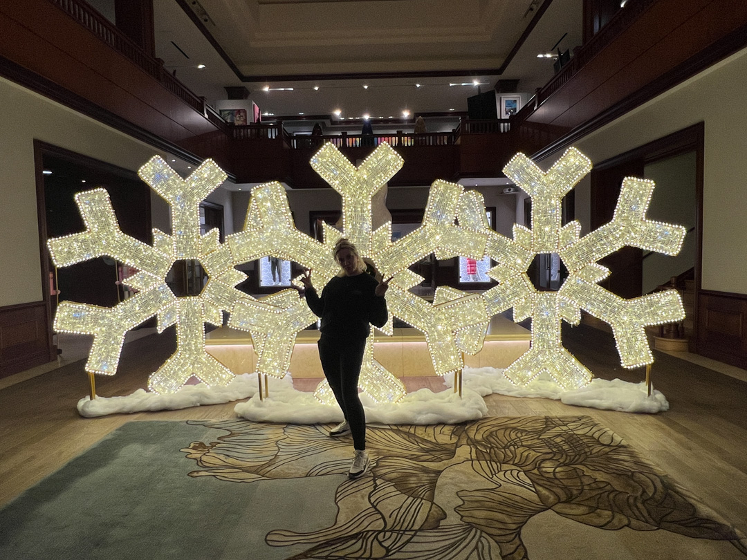 Person posing in front of four large illuminated snowflake decorations indoors.