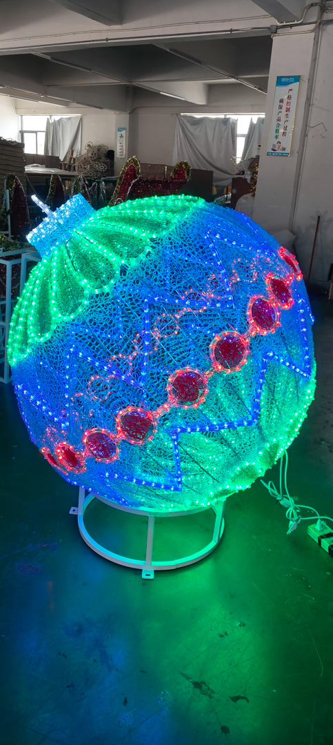 Large decorative lighted spherical ornament with green, blue, and red LED patterns on a stand indoors.