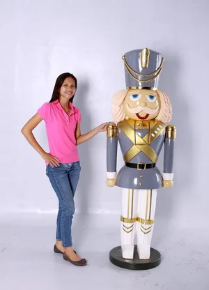 Woman in pink shirt and jeans standing next to a tall wooden nutcracker soldier statue with a blue and gold uniform.
