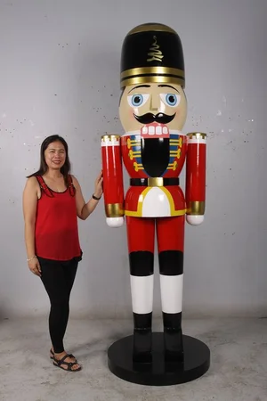 Woman standing next to a large colorful nutcracker figure wearing a red, white and black uniform with a black hat.