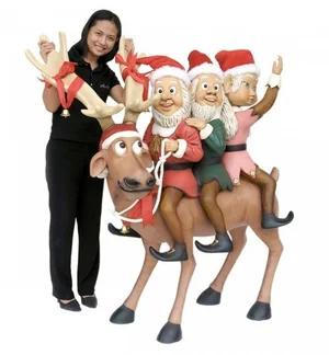 Woman standing next to a large reindeer statue with three Elf figures riding on its back.