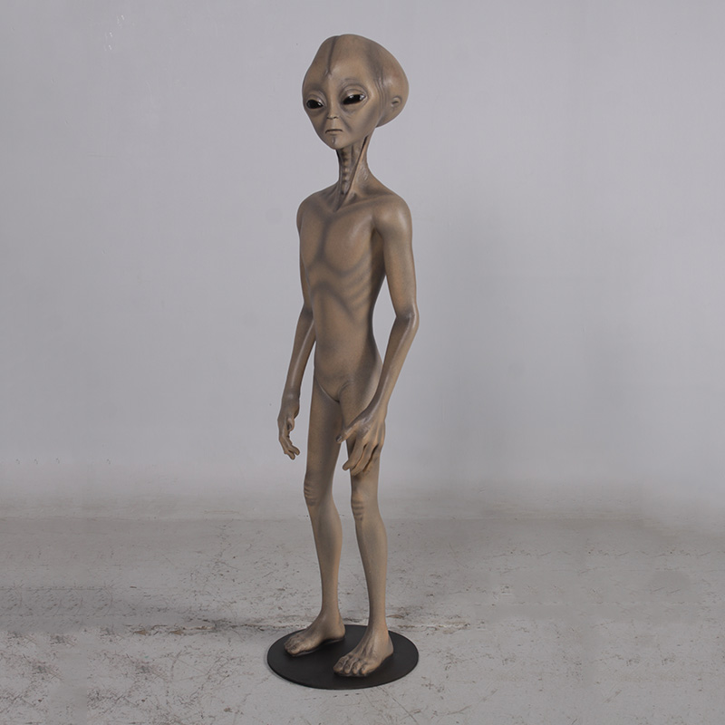Brown alien figure with large head and big black eyes standing on a black circular base.