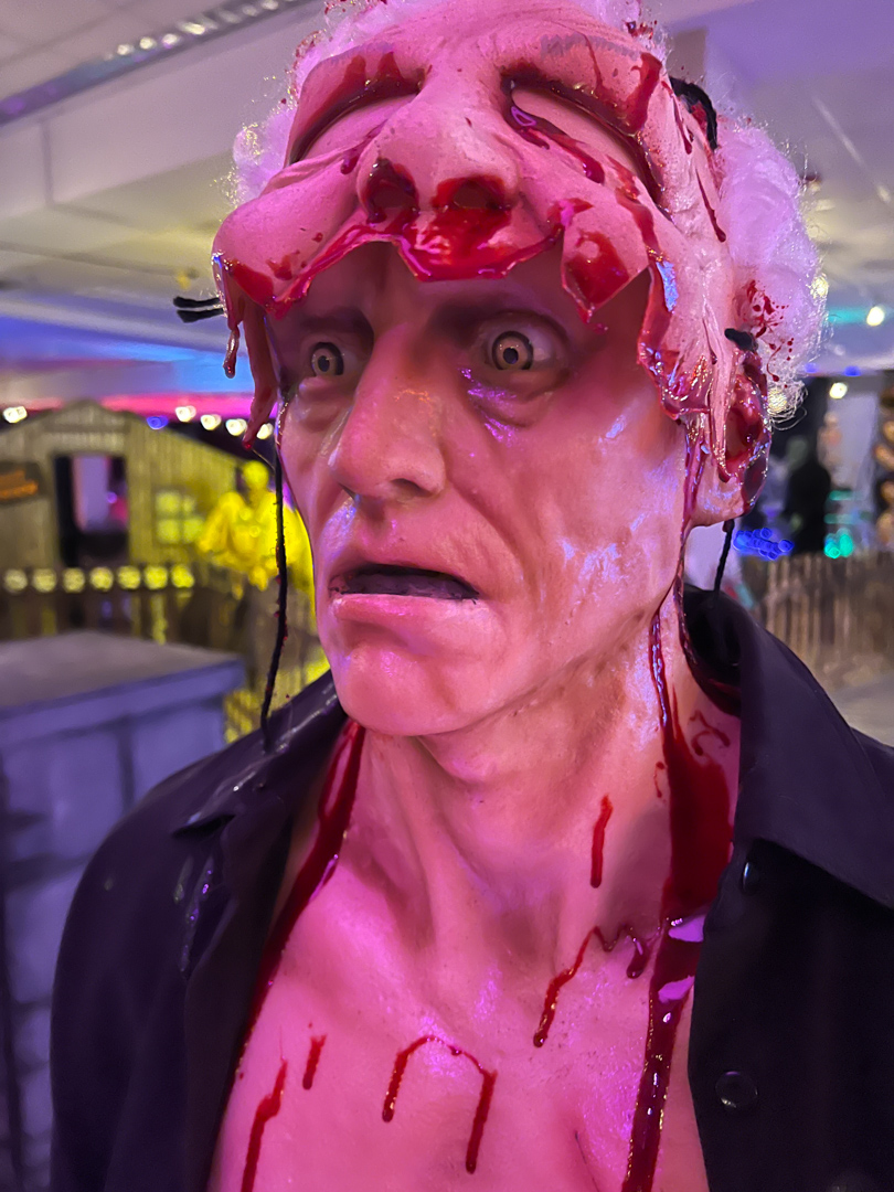 Close-up of a lifelike zombie figure with blood and exposed skull wearing a black shirt indoors.