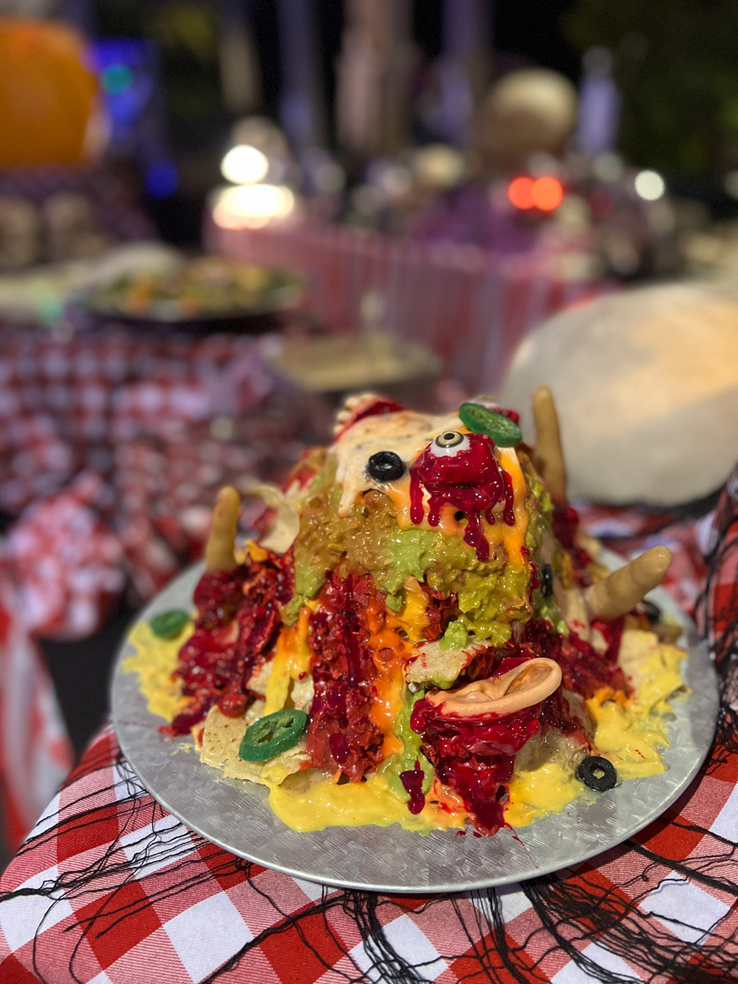 Halloween-themed nachos with colorful sauces and fake body parts on a silver plate