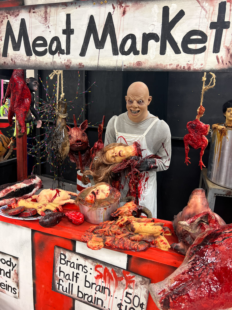Mannequin butcher at a gruesome meat market display with fake severed heads and body parts.