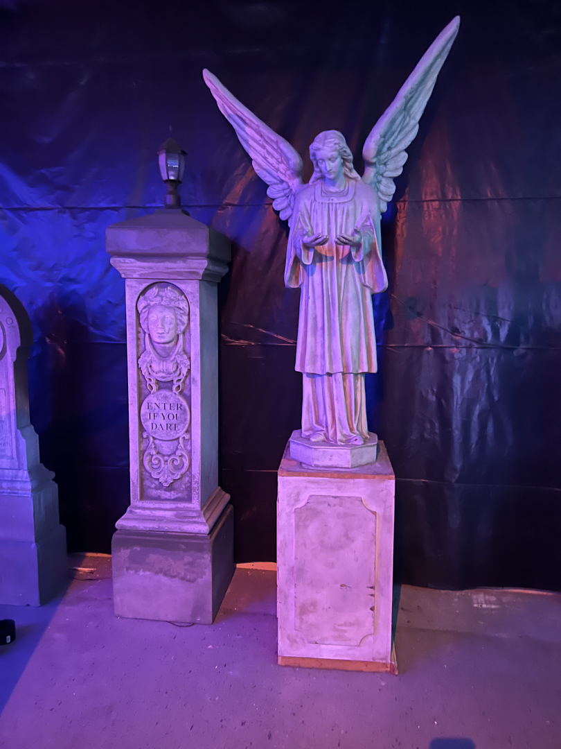 Stone statue of an angel with wings and a pedestal beside a pillar that reads 'ENTER IF YOU DARE'.