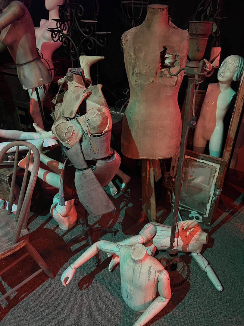 Vintage dress forms, mannequins, and wooden articulated artist models in dim lighting.
