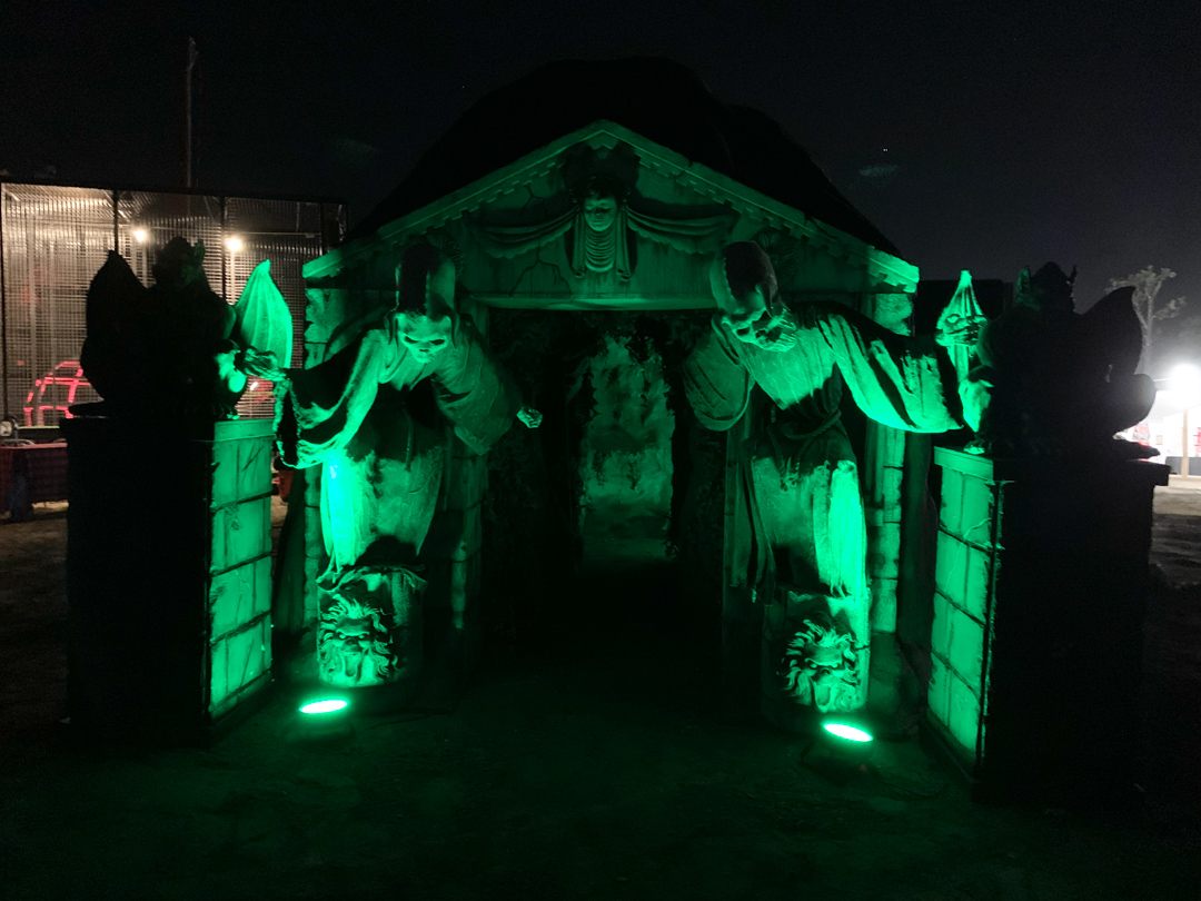 Gothic entrance with two green-lit angel statues leaning forward at night.