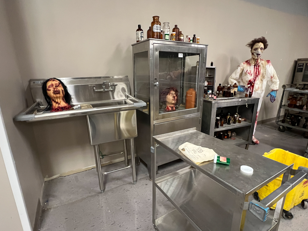 Room with anatomical props including bloody severed heads and a mannequin in a blood-stained lab coat.