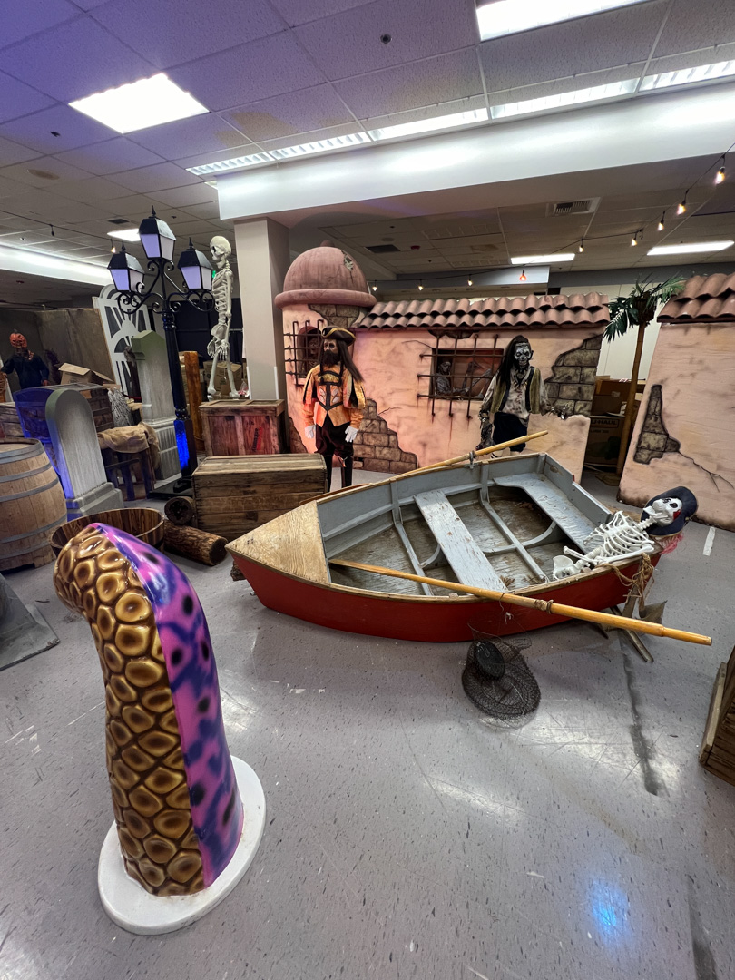Indoor pirate-themed scene with a skeleton in a boat, pirate figures, crates, barrels, and a tentacle prop.