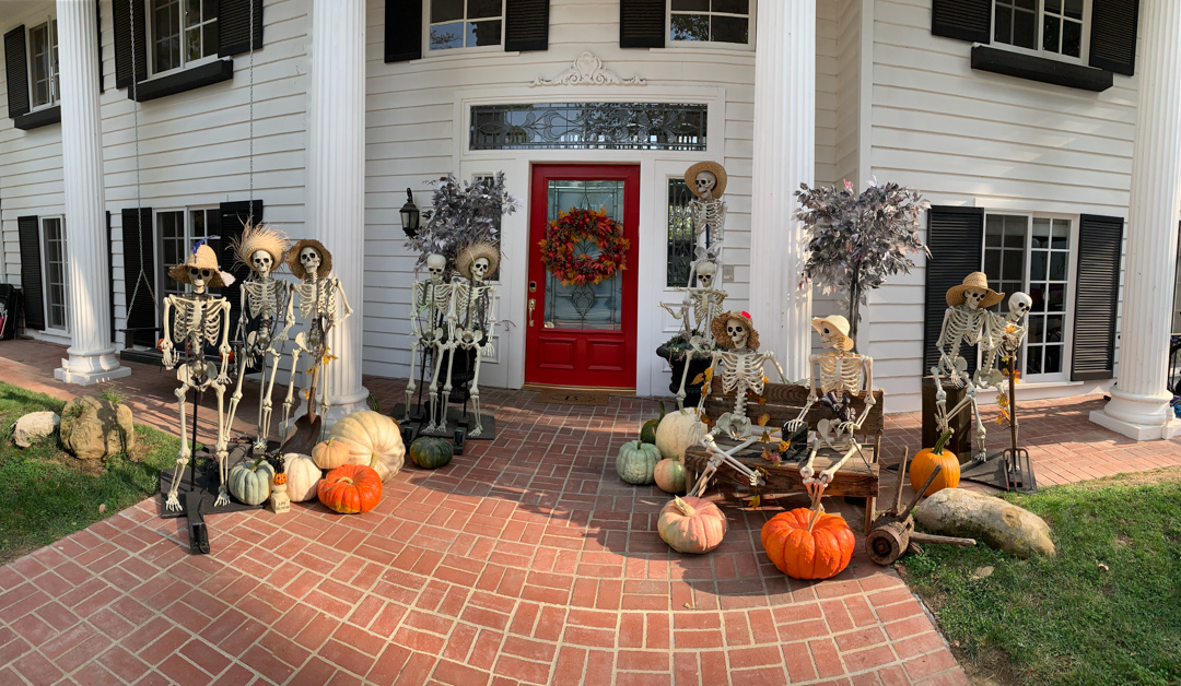 Skeletons and pumpkins decorate the brick porch of a white house.
