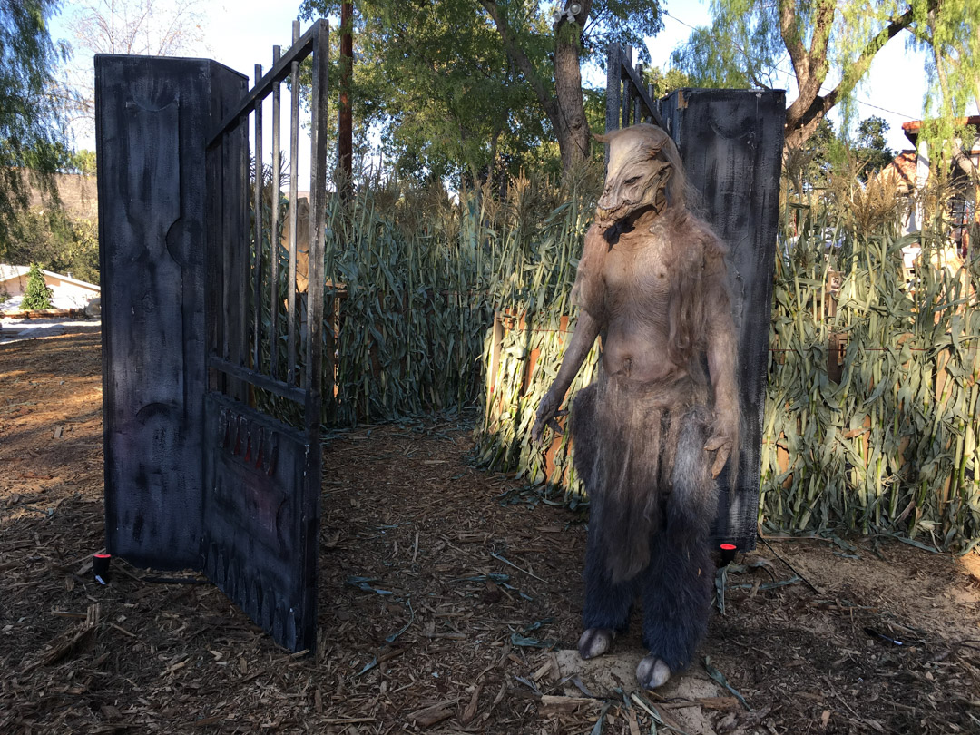 A large Bigfoot figure emerges between dark wooden gates in a wooded setting.	A large Bigfoot figure emerges between dark wooden gates in a wooded setting.