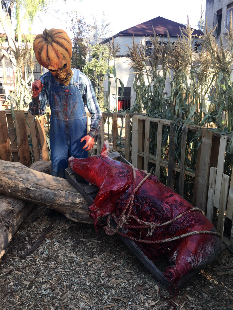 A large Bigfoot figure emerges between dark wooden gates in a wooded setting.