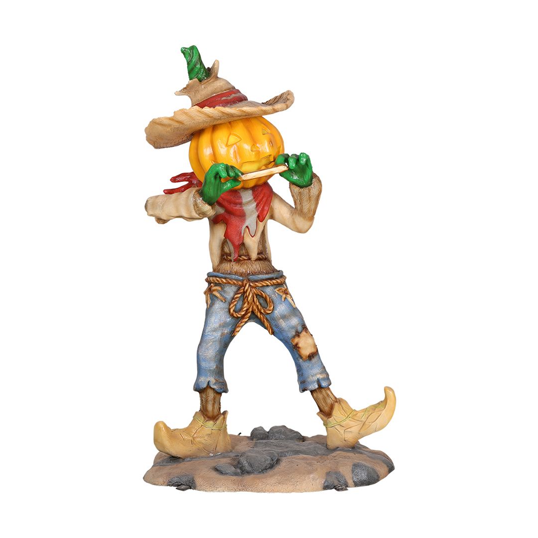 Figurine of a scarecrow with a pumpkin head playing a flute, wearing a hat, scarf, patched jeans, and boots.