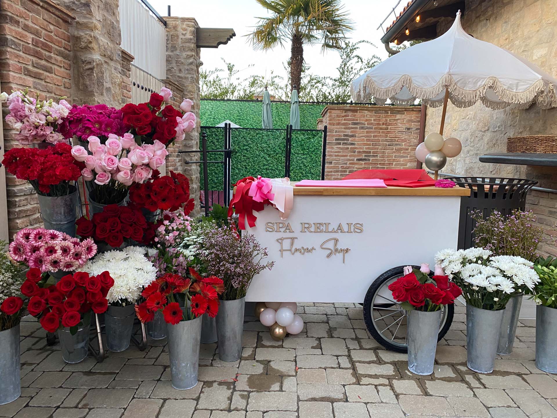 Outdoor flower shop cart with bouquets of red, pink, white flowers beside stone walls on a stone floor.