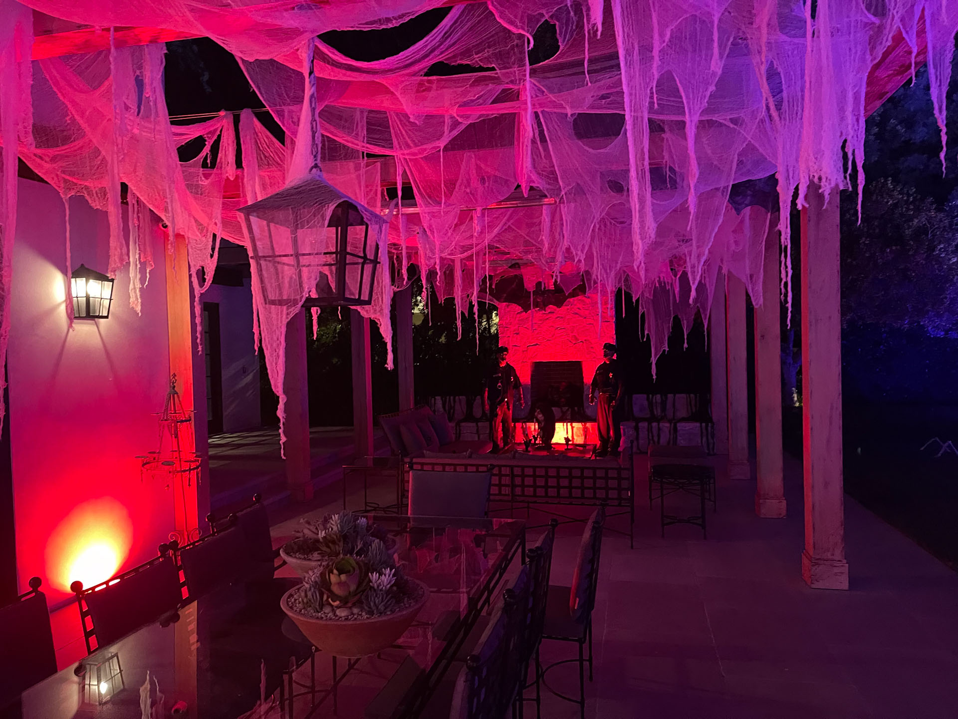 Eerie outdoor seating area with hanging web decorations lit by red and purple lights at night.