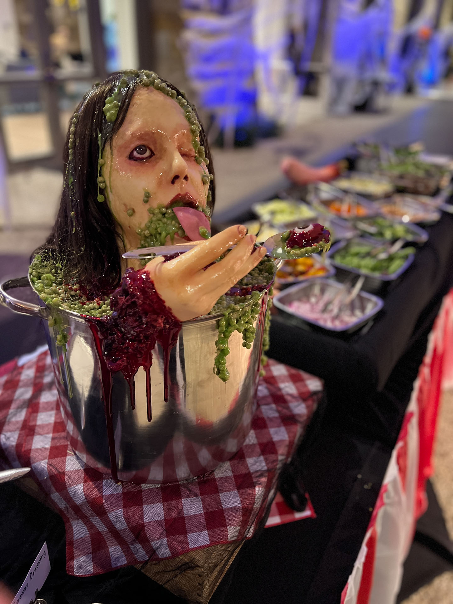 Halloween decoration of a severed head in a pot with green slime and a hand holding a spoon with an eyeball.
