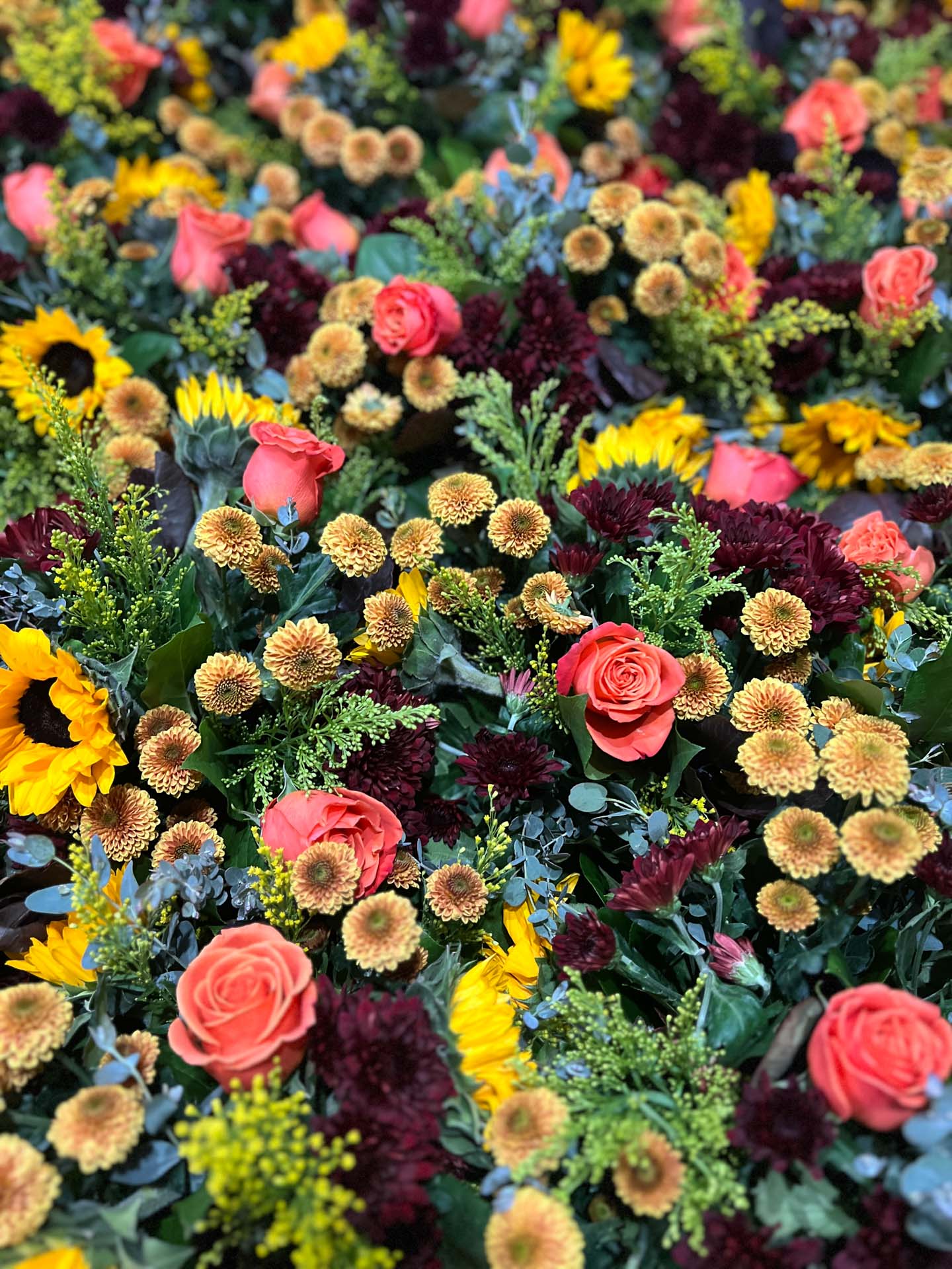 Dense arrangement of pink roses, yellow sunflowers, and small cream and burgundy flowers with green foliage.
