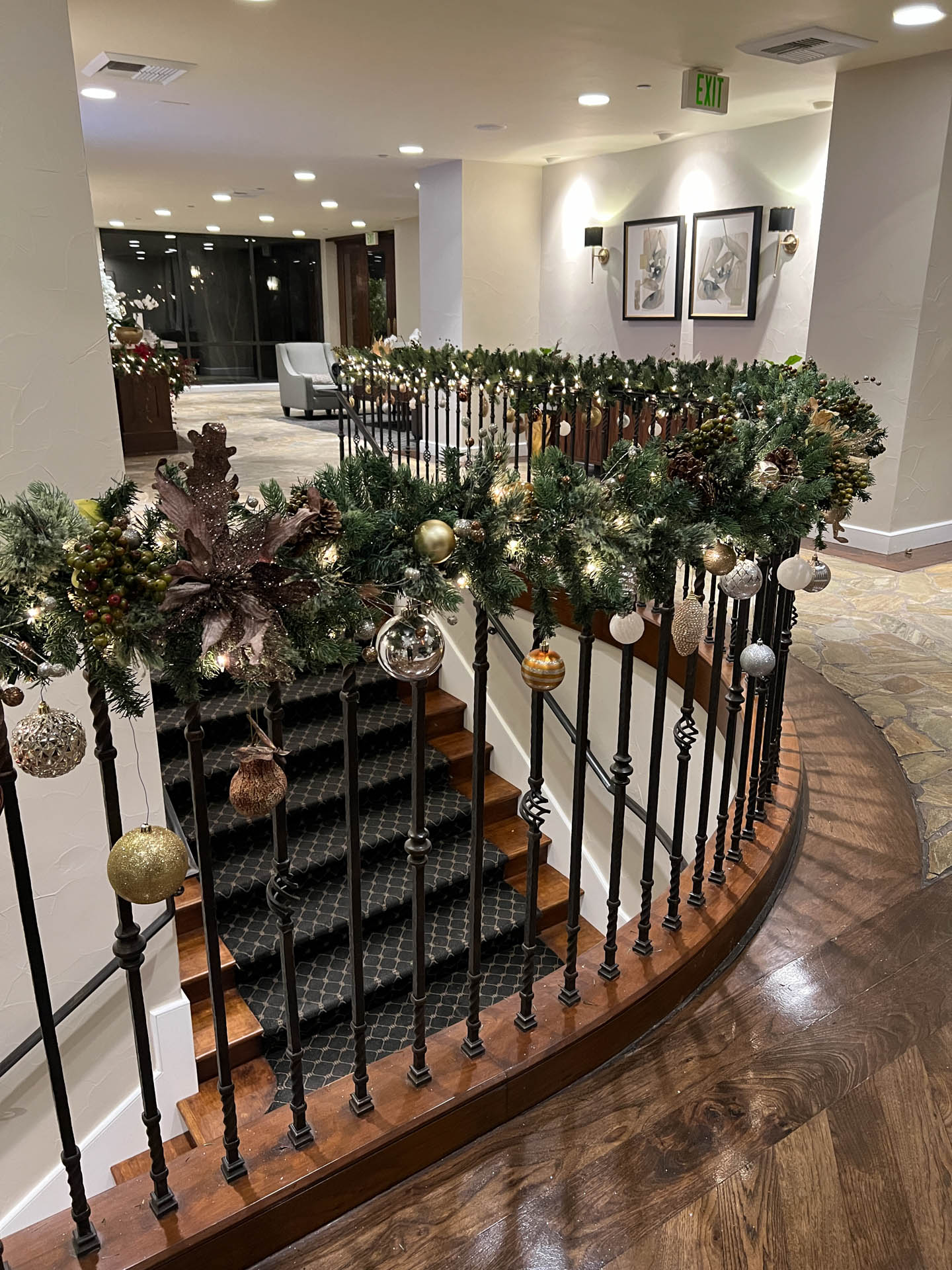 Curved staircase railing decorated with green garland and gold, silver, and brown Christmas ornaments.