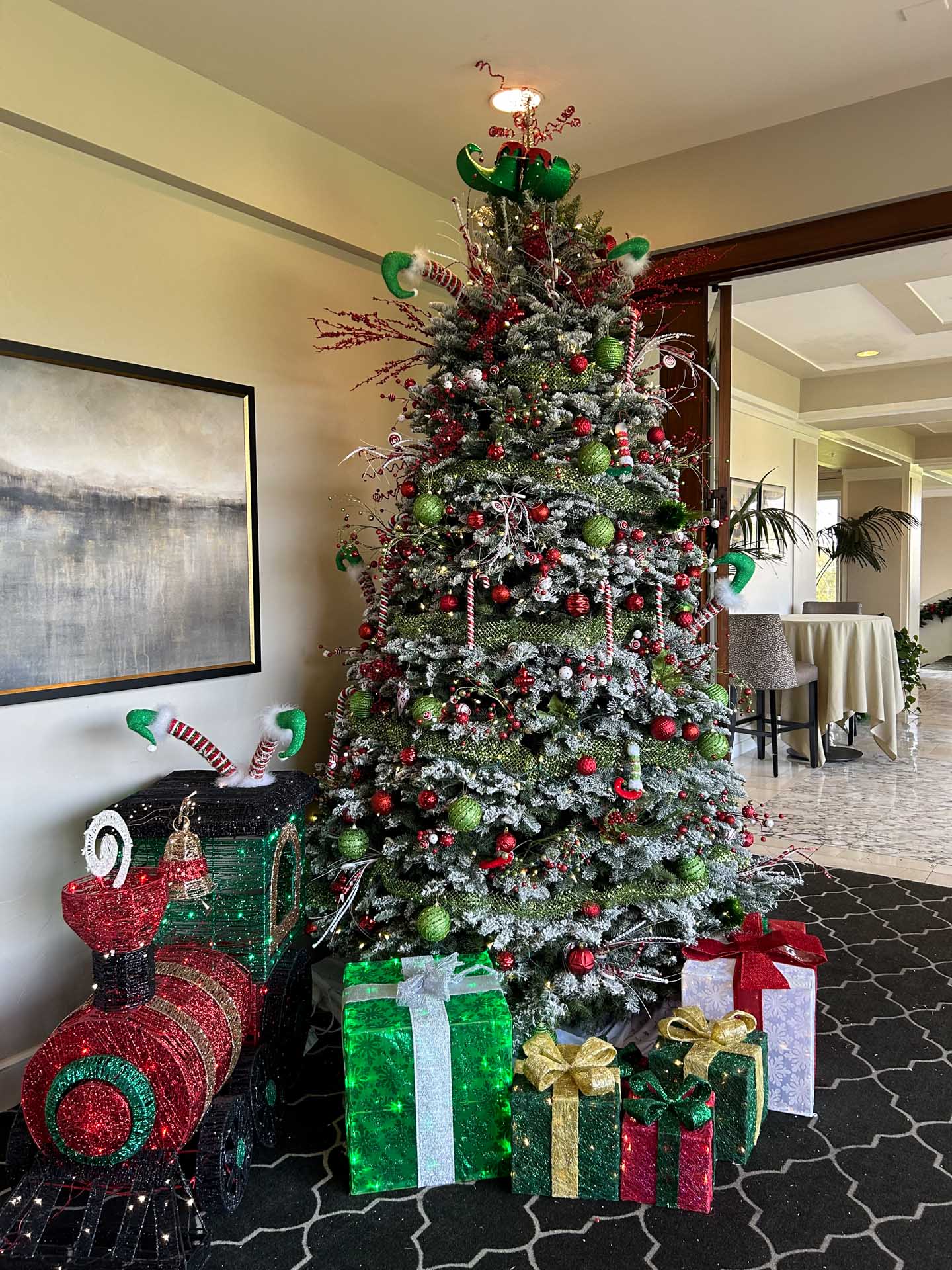 Decorated Christmas tree with red and green ornaments, presents, and a light up train decoration beside it.
