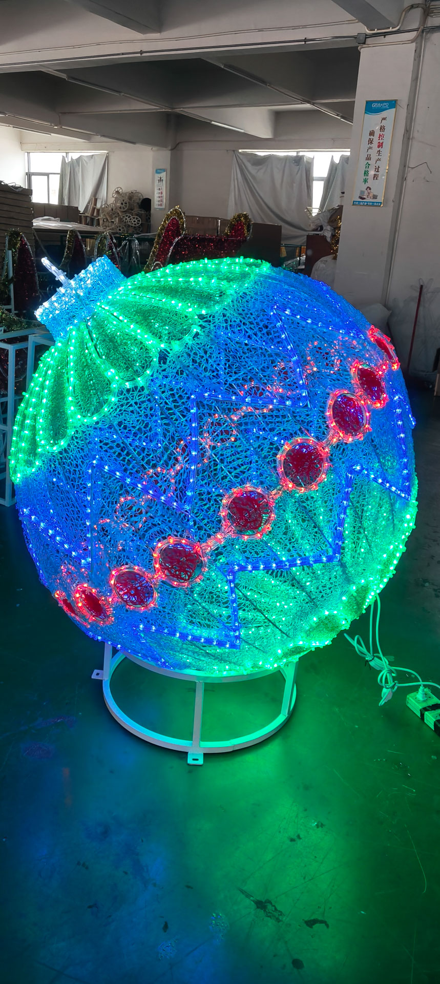 Large decorative lighted spherical ornament with green, blue, and red LED patterns on a stand indoors.