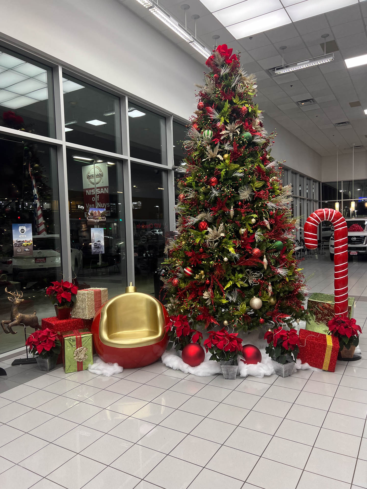Large decorated Christmas tree with red poinsettias, gifts, candy cane, and a gold and red ornament chair.