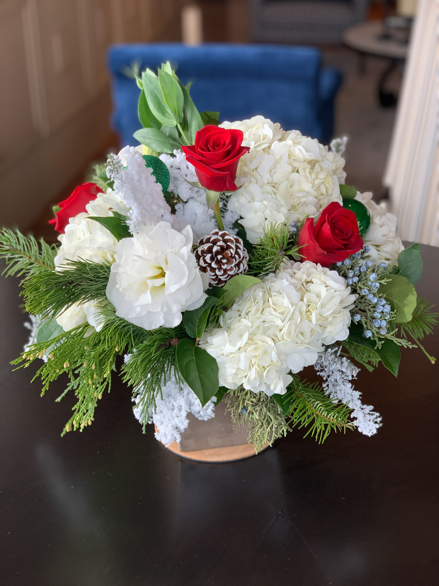 Floral arrangement with red roses, white hydrangeas, greenery, pinecones, and snowy accents.