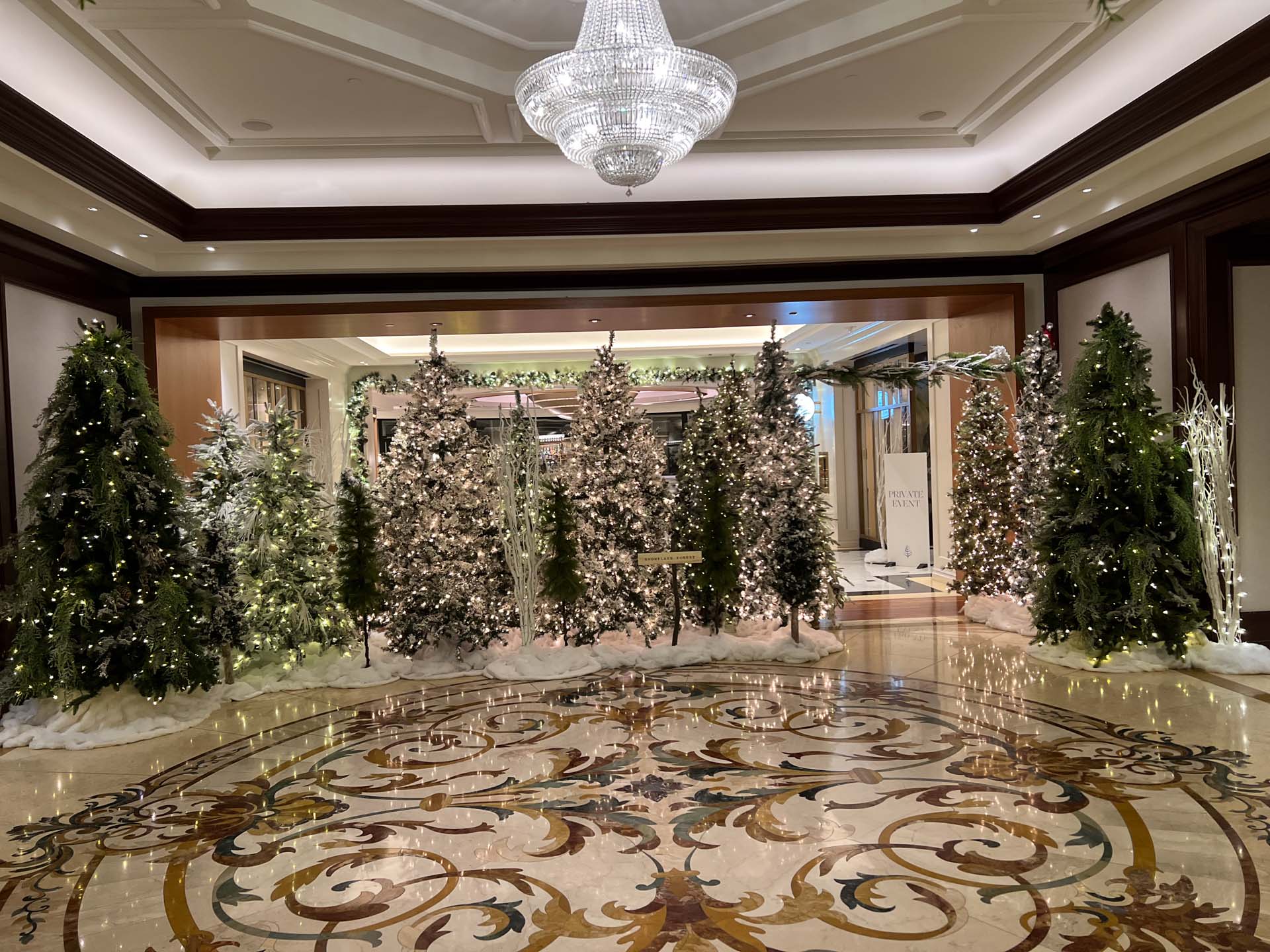 Luxury lobby with ornate floor and a row of decorated Christmas trees with lights and artificial snow.