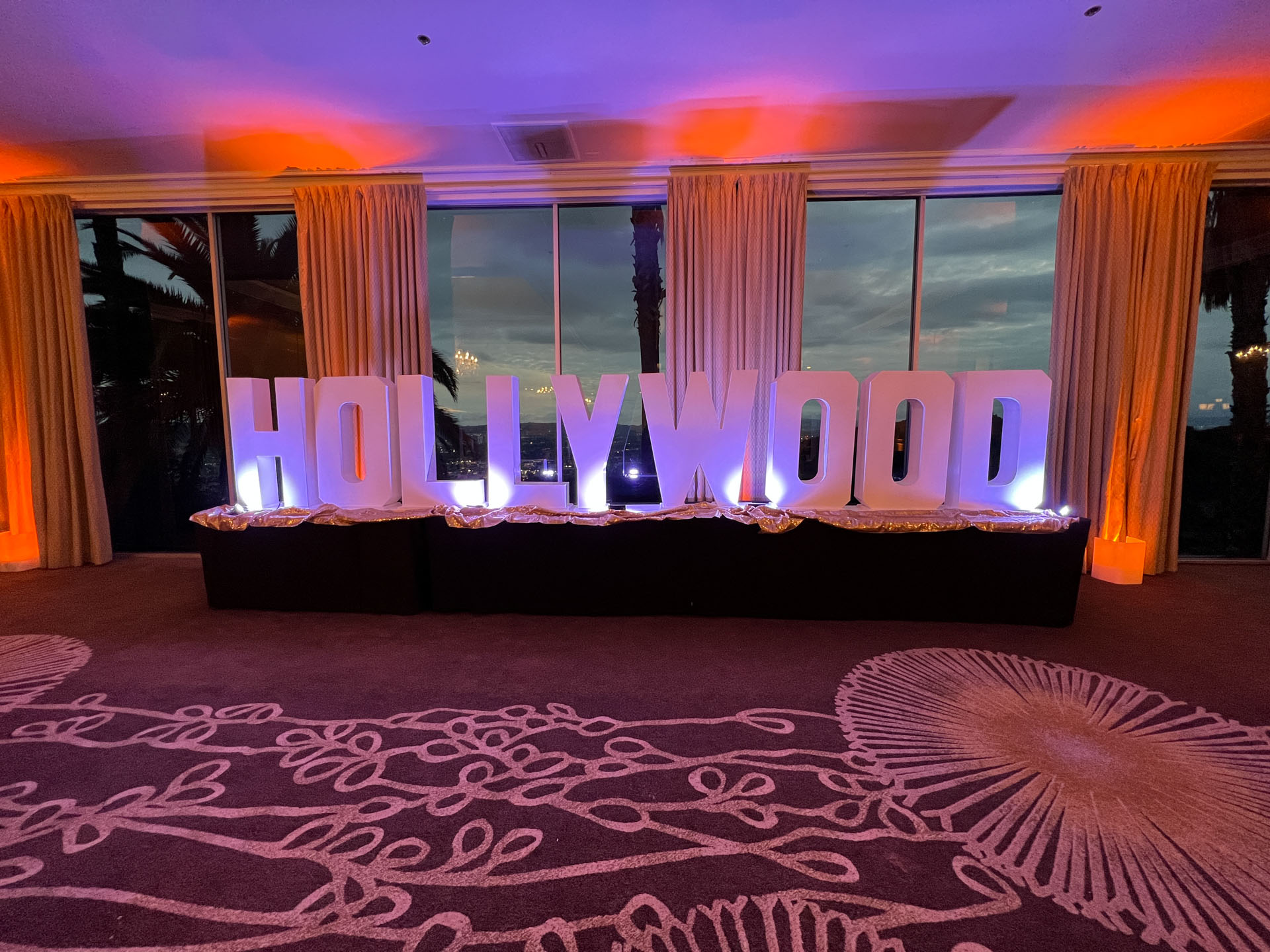 Large illuminated letters spelling 'HOLLYWOOD' in a dimly lit room with windows and curtains.