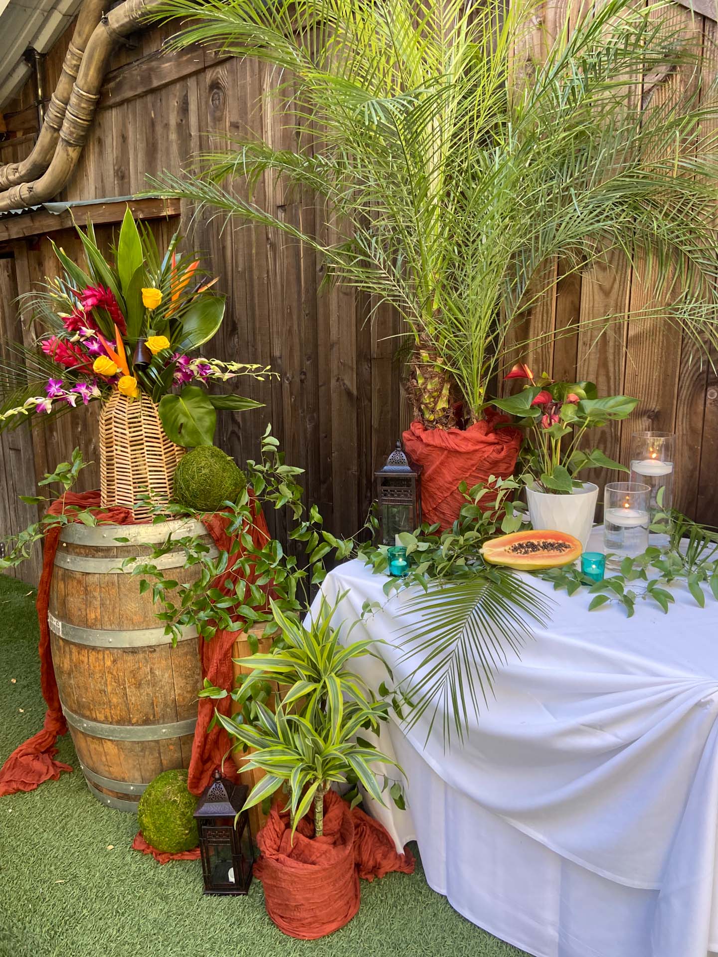 Wooden barrel and table decorated with tropical plants, flowers, candles, and a half papaya with seeds.