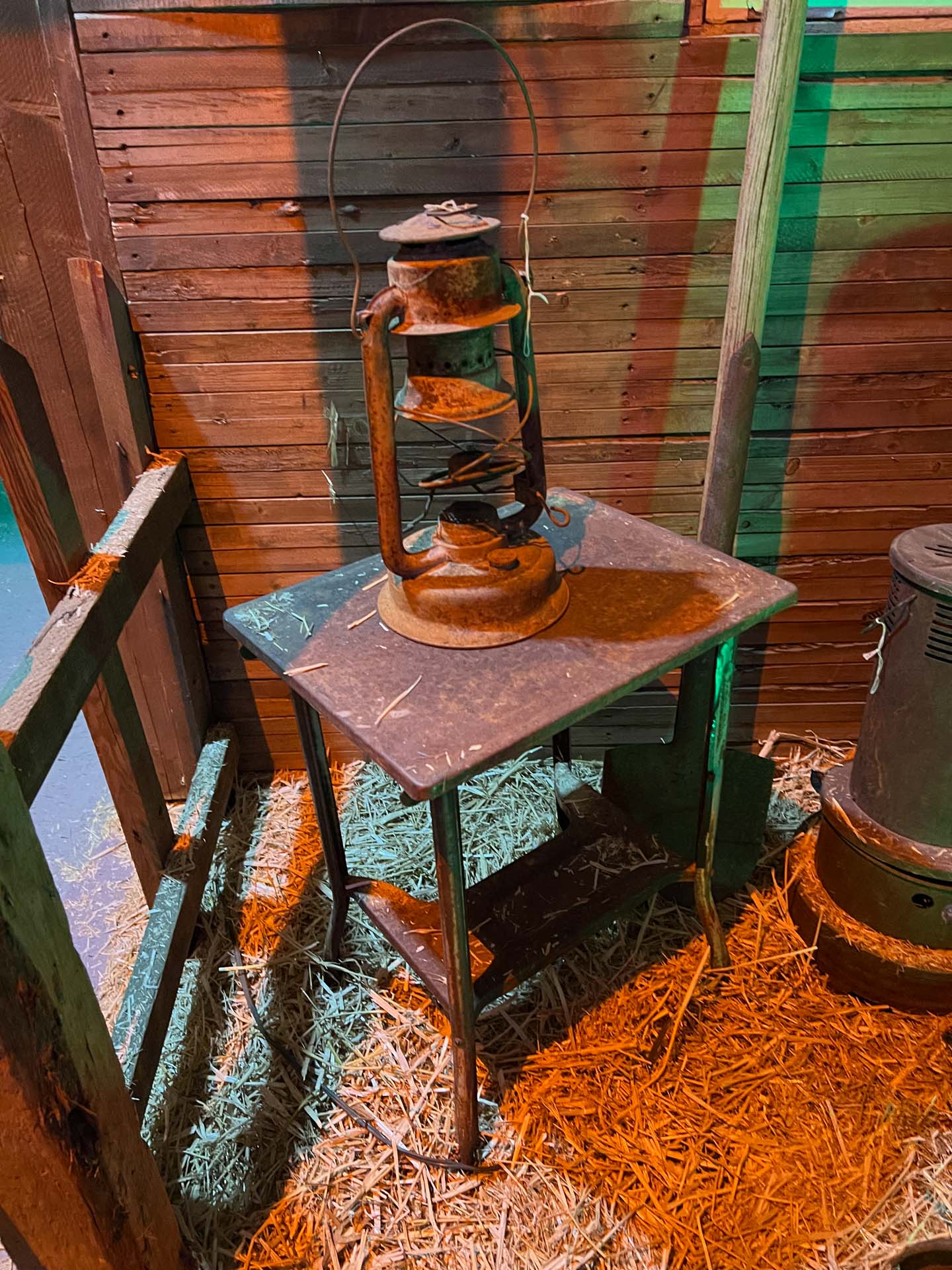 Rusty old lantern on a metal table with hay scattered on the floor against wooden walls.