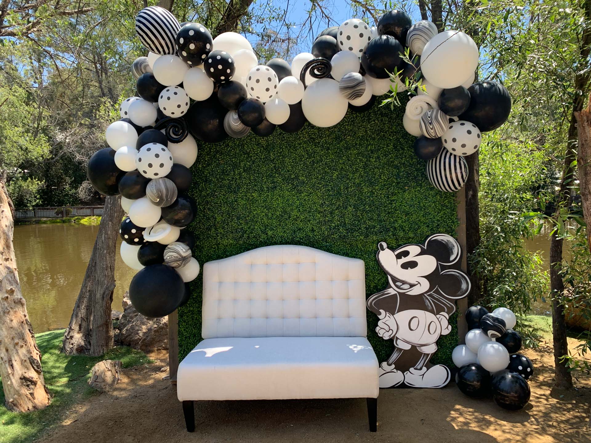 White sofa in front of green hedge with black and white balloons and a Mickey Mouse cutout.