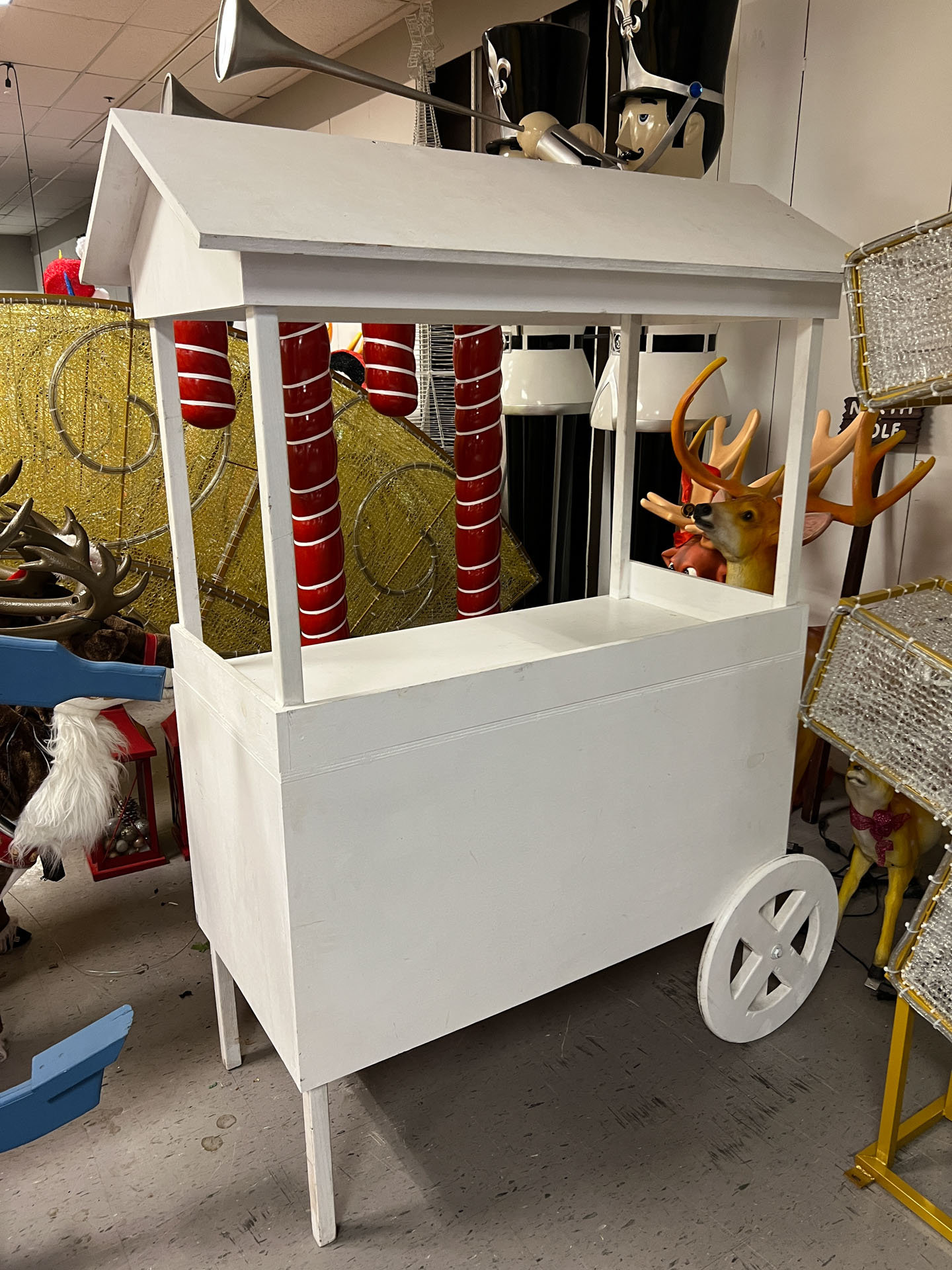 White wooden pushcart trolley with roof, standing indoors near other holiday decorations.