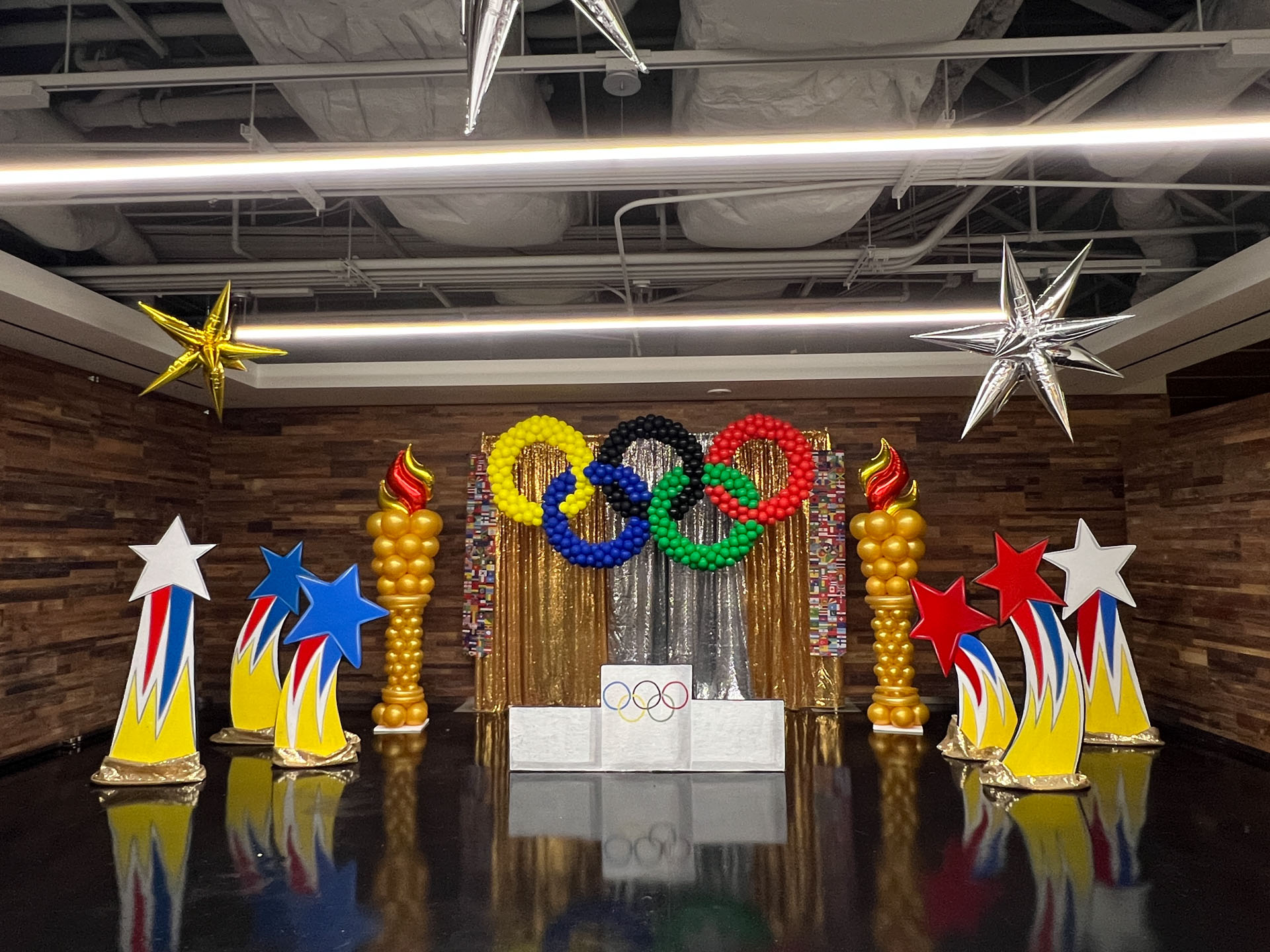 Olympic-themed room with balloon rings, torch balloons, star-shaped decorations, and a winners' podium.