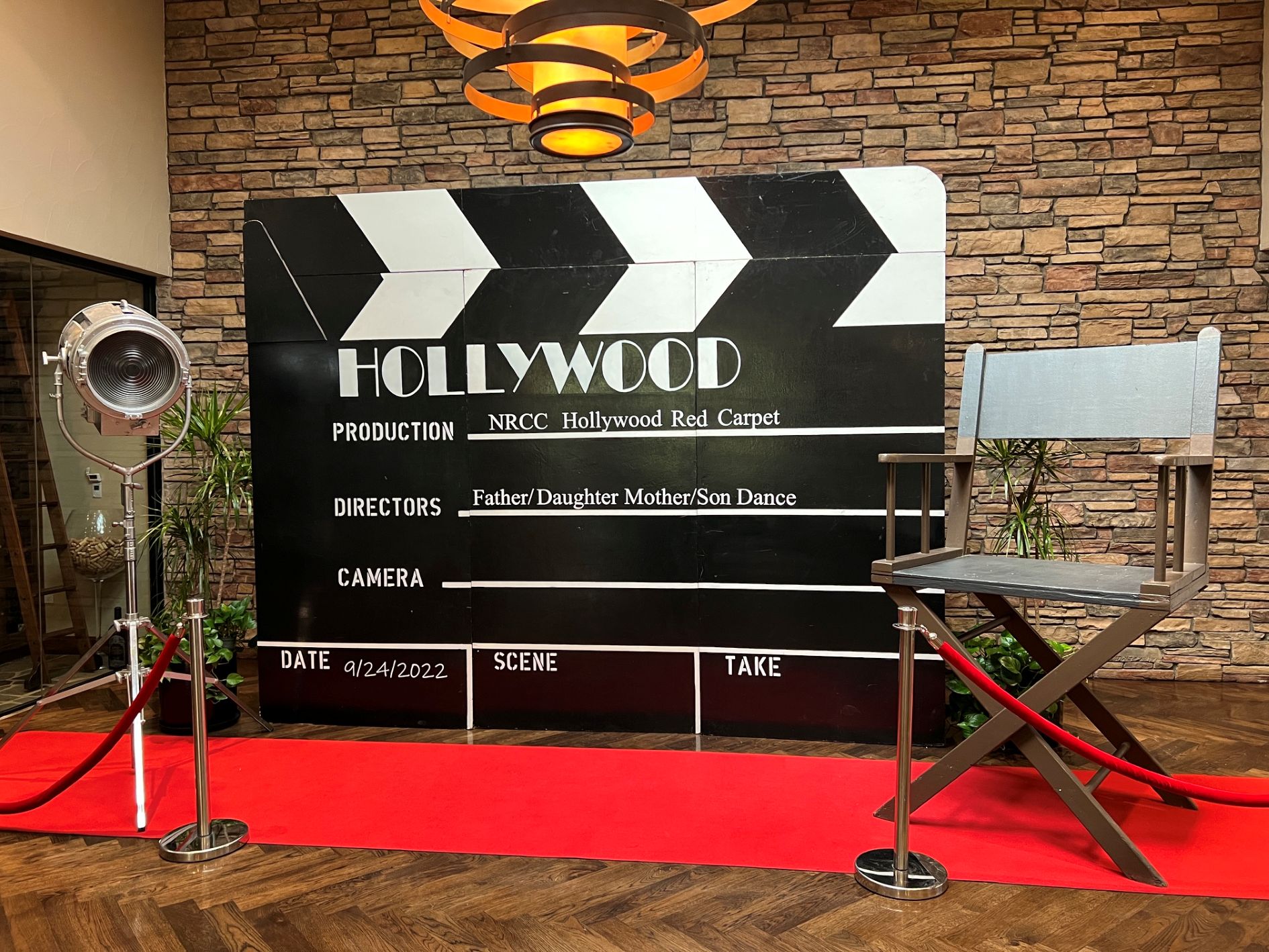 Large Hollywood clapperboard display with red carpet, spotlight, and giant director's chair indoors.