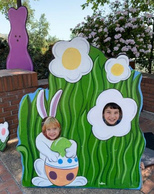 Boy and girl posing for photo in cutout of easter flower and easter bunny holding an easter egg with grass.