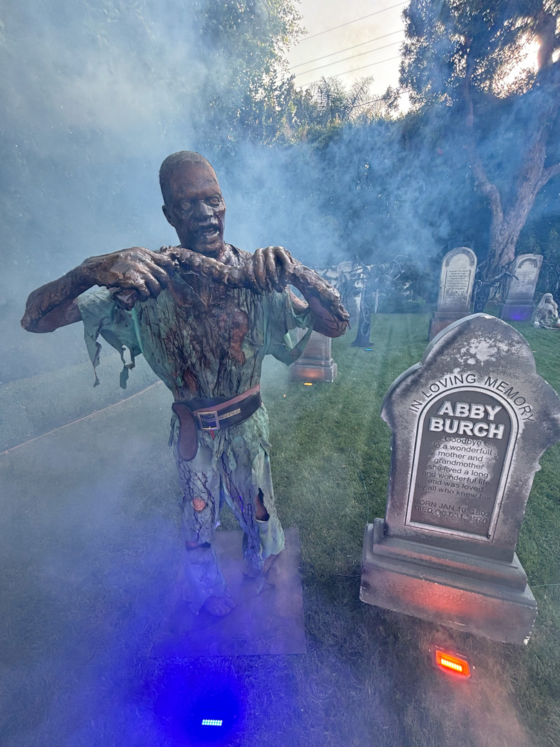 Zombie decoration holding a body part near a gravestone in a foggy Halloween display.
