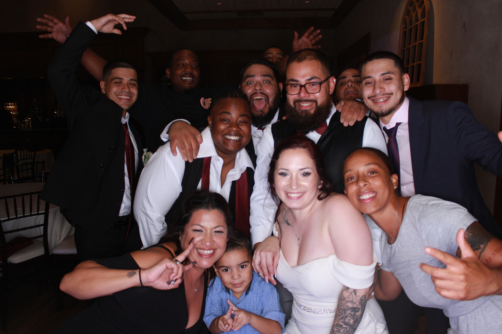 Large group of wedding guests posing and laughing together during an indoor reception.