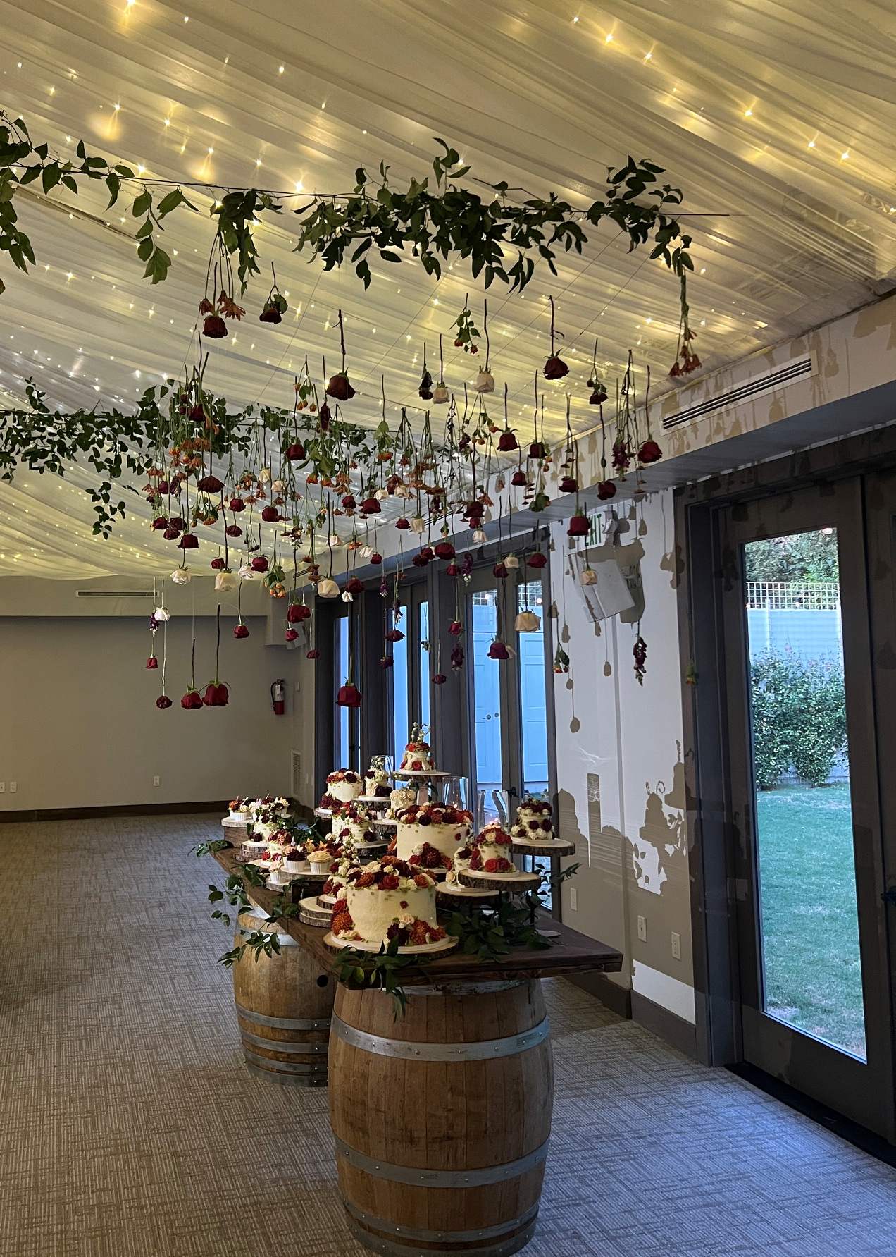 Hanging red and white roses suspended above a rustic wedding dessert display arranged on wooden barrels.